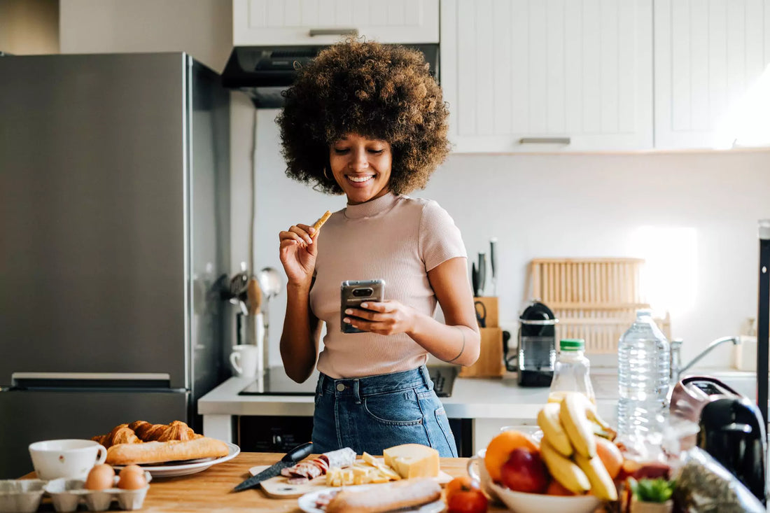 A woman checking her phone in the kitchen, just starting to break her fast.
